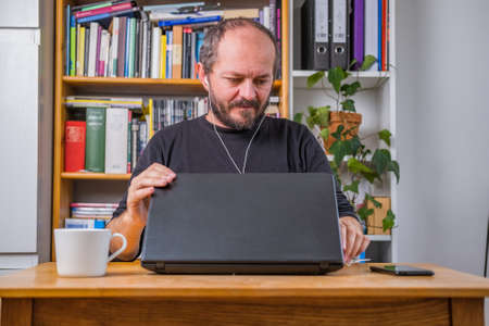 Man working online from home, with earphones, closing computer laptop after online video meetingの写真素材