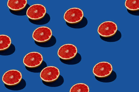 Sunlit red grapefruit pattern on a blue background. Minimal creative summer layout.の写真素材