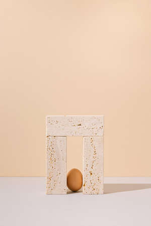 Single egg standing in a travertine marble blocks doorway on a beige and gray background. 2021 Easter unique still life arrangement. Surreal retro creative architecture concept.の写真素材