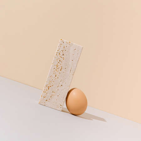 Raw egg pushing travertine marble block uphill. Beige and gray background. 2021 Easter unique still...