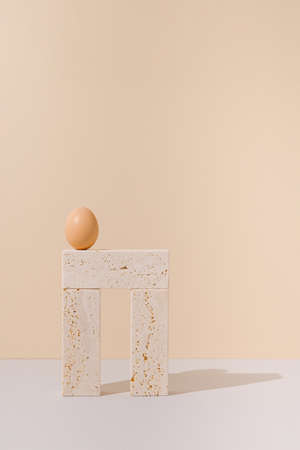 Egg on top of travertine marble blocks structure on a beige and gray background. 2021 Easter unique still life concept. Surreal retro food arrangement.の写真素材