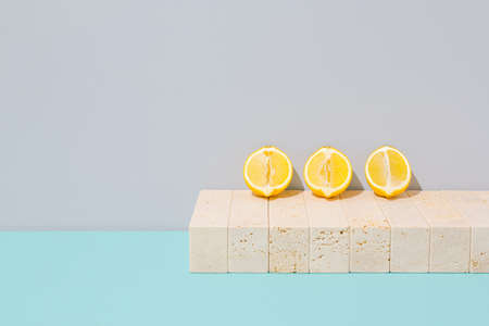 Group of lemons lounging by the sea on marble blocks. Yellow summer fruit arrangement against cyan blue and gray background. Surreal vintage swimming pool concept. Pastel colored retro beach scene.の写真素材