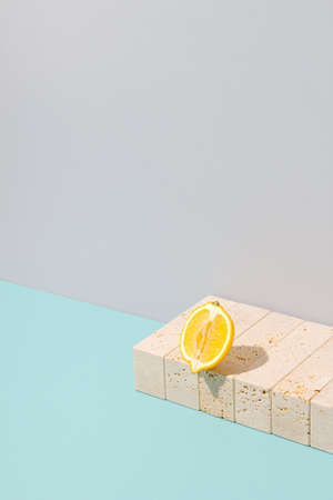 Sliced lemon sitting on the edge of swimming pool. Yellow summer fruit arrangement against cyan blue and gray background. Surreal marble stone vintage concept. Sunlit pastel colored retro beach scene.の写真素材
