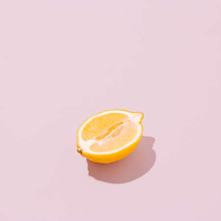 Lemon half on a pale pink background. Sunlit vintage yellow summer fruit with shadow. Retro beach food aesthetic layout.の写真素材