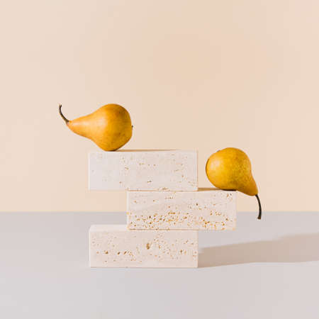 Yellow pears balancing on travertine marble blocks structure against gray and beige background. Creative summer fruit arrangement. Minimal retro styled surreal food art concept.の写真素材