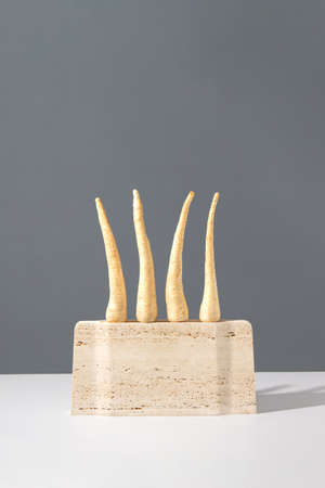 Unique parsley roots still life produce composition. Abstract travertine marble sculpture with raw vegetables on a grey background. Surreal retro minimal creative food concept.の写真素材