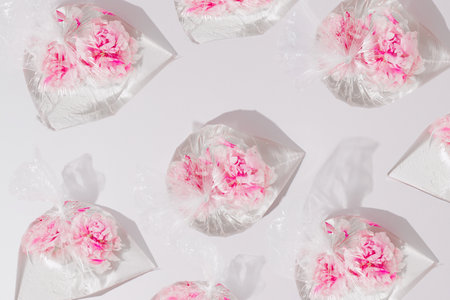 Pink peony flowers inside water filled transparent nylon bags on a grey background. Sea plastic pollution prevention idea. Creative environment saving pattern.の写真素材