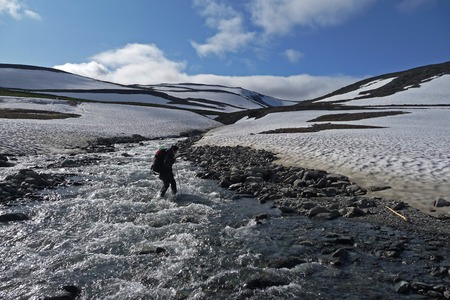 Tourist passes mountain river, around the snow against the blue skyの写真素材