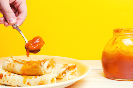 Traditional Ukrainian or Russian pancakes. Shrovetide Maslenitsa. Traditional dishes on the holiday Carnival Maslenitsa Shrovetide, hand with a spoon of jam, apricot  jar of jam. place for text



の写真素材
