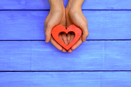 Red wooden heart in hands on a blue wooden backgroundの写真素材