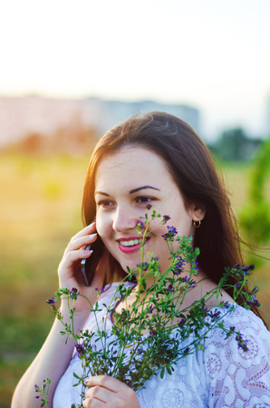 happy young brunette woman talking on the phone with flowers in her hands and smiling. portrait. close-up photo

の写真素材