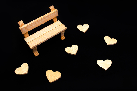 A wooden bench and hearts. A place for visiting lovers. Empty bench. Frustrated date. Disappointment, broken heart. A black background. Toy bench. The concept of a meeting place for lovers.の写真素材