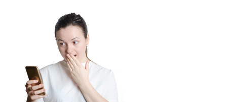 young beautiful brunette girl looking surprised at the phone on white isolated backgroundの写真素材
