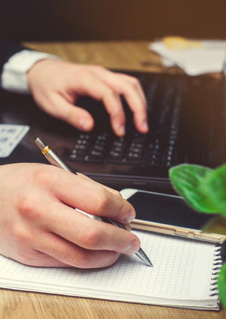 Hand of businessman in suit on keyboard filling and signing with a silver pen documents. Finance and accounting business background. wood tableの写真素材