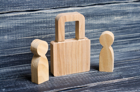 Two people stand near a padlock and keep secrets, information, entrance. Wooden figures of persons carry guards from wicked men, spies. The concept of the preservation of secrets, information and values.の写真素材