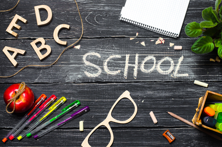 A student's desk on a school board, a dark wooden background made of boards. Concept of education and school. Inscription school. The office is on the table. Top view, space for text. Workplace.の写真素材