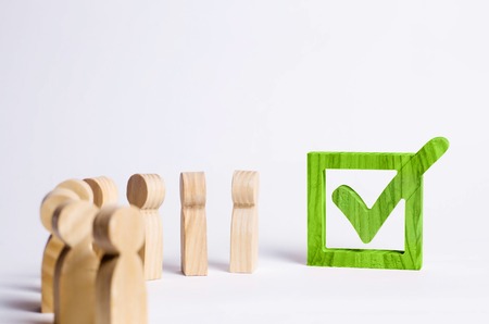 wooden human figures stand together next to a tick in the box. The concept of elections and social technologies. Volunteers, parties, candidates, electorates. Selective focus.の写真素材