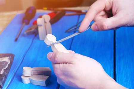 Men's hands make a hand-made article of wood on the background of a blue table with tools. Work at home and in the workshop. Wooden figures of people. Concept of carpentry, useful occupation.の写真素材