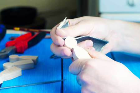 The master processes the wood with his hands. Working hands on a blue background with tools. Creation of domestic crafts made of wood. Small wooden figures of people. Concept work yourself. DIYの写真素材