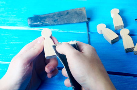 The master processes the wood with his hands. Working hands on a blue background with tools. Creation of domestic crafts made of wood. Small wooden figures of people. Concept work yourself. DIYの写真素材