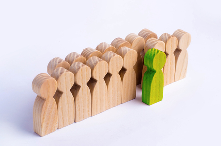 The chosen person among others. A human figure of green color stands out from the crowd. Wooden figures of people. A talented worker, a successful choice. Promotion. Concept of search for worker.の写真素材