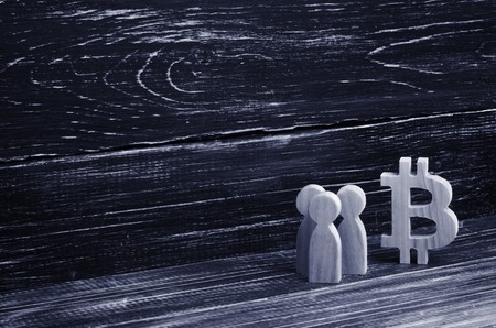 Wooden figures of people are standing near a bitcoin on a black background. Crypto currency, blockchain technology. The collapse and rise cost of bitcoin. Mining farms, miners, stock exchange cryptsの写真素材