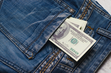 Banknotes of a hundred dollars with a portrait of Franklin peep out of the pocket of jeans trousers....