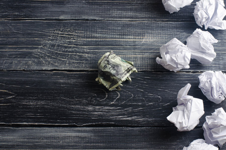 A crumpled dollar on a table next to white paper balls. The process of thinking and finding new business ideas, profitable solutions. Attraction of investments and creation of businessの写真素材