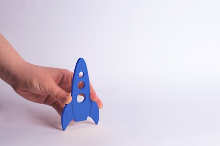 Wooden blue rocket in hand on a white background. A man is playing with a rocket. Minimalism, space travel and tourism, commercial rocket launches into space. The conquest of other planetsの写真素材