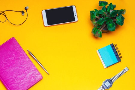 working space with a notebook, pen, clock, telephone, headphones on a yellow background. place for text. The working space of a freelancer, journalist, writer. On a bright yellow background. Top view.の写真素材