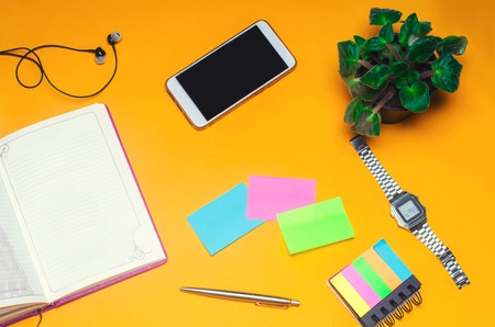 working space with a notebook, pen, clock, telephone, headphones on a yellow background. place for text. The working space of a freelancer, journalist, writer. On a bright yellow background. Top view.の写真素材