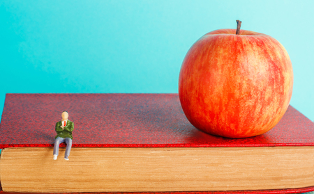 man is sitting on a book. the concept of education. apple and books, blue background, place for text, back to school, copy spaceの写真素材
