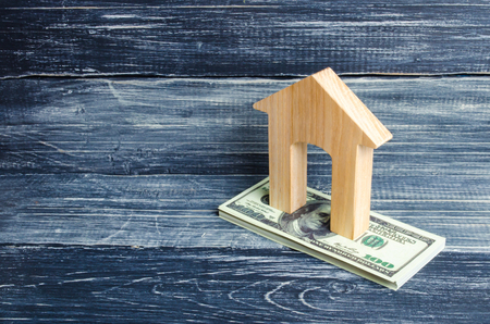 A wooden house stands on a stack of dolor banknotes. The concept of buying and selling immovability, rent of apartments. Credit and mortgage, affordable housing. Utilities paymentsの写真素材