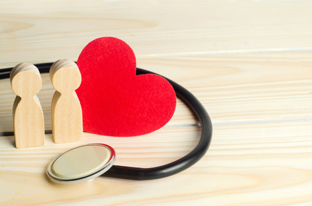 the concept of family medicine and insurance. figures of people, stethoscope and heart on a wooden backgroundの写真素材