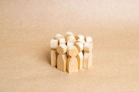 A crowd of wooden figures of people stands in a pile on a beige paper background. The concept of cohesion and cooperation. Frightened people, herd behavior. Team, target audienceの写真素材