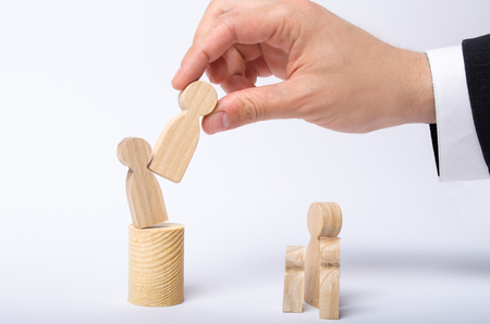 The man's hand of a businessman in a business suit holds a wooden figure of a man in his hand and moves another figure from his post. concept of firing an employee, the replacement of staff.の写真素材