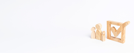 Three wooden human figures stand together next to a tick in the box. The concept of elections and social technologies. Volunteers, parties, candidates, constituency electorates. Human rights. Bannerの写真素材