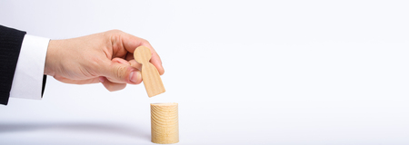 A man's hand puts a person's figure on top of his new post. A businessman appoints a person to a managerial position. Recruitment and leadership position. Human resources, headhunters Bannerの写真素材