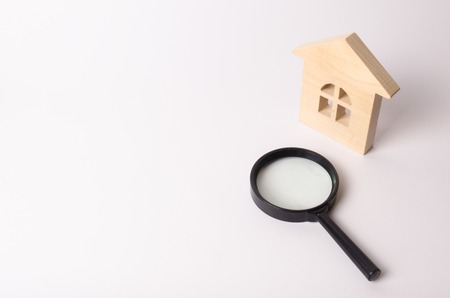Wooden house and a magnifying glass on a white background. The concept of finding a house, buying or renting an apartment. Realtor services. Search for a new home. Real estate market.の写真素材