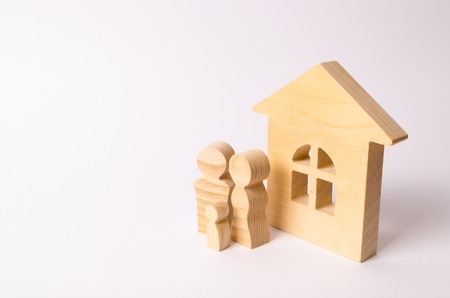 Figures of people stand near a wooden house on a white background. A young family is standing near their house. The concept of buying a home. The property. Family happiness. Unit of society.の写真素材
