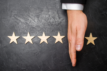 The hand of the businessman separates the fifth star from the other four. The loss of the fifth star, the fall in rating and recognition.の写真素材