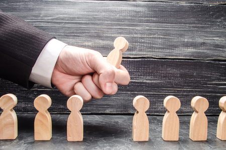The hand of a businessman grabs a wooden figure of a man from a number of workers.の写真素材