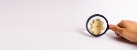 Hand with the magnifying glass is aimed at the wooden wheel gear. concept of studying the technological process and industry, the production chain, the manufactory. Search for parts and spare parts.の写真素材