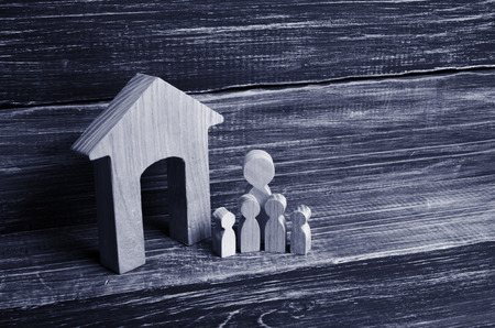 Big family is standing near the house. Wooden figures of persons stand near a wooden house. The concept of a couple in love, cohabitants, parents, buyers and sellers at home. They live in the houseの写真素材