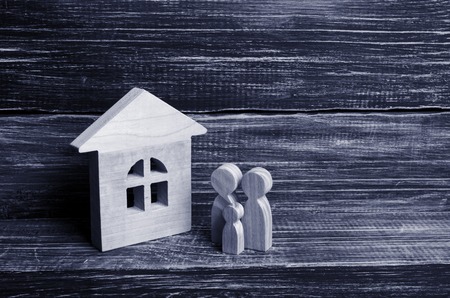 A young family with children is standing near a wooden house. The concept of a strong family, the continuation of the family. Loans for the purchase of affordable housing. A new house for the familyの写真素材