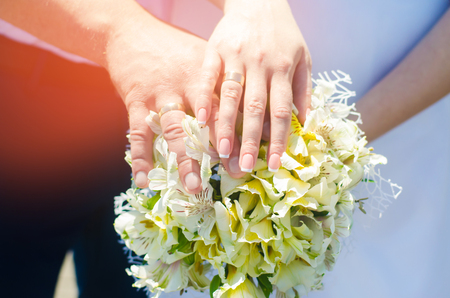 Close-up Bride and groom's hands with wedding rings and bouquet. Love and marriage. Wedding accessories and decor on the background of the riverの写真素材