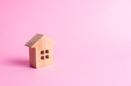 A small wooden house stands on a pink background. The concept of buying and selling real estate, renting. Search for a house. Affordable housing, credit and loans. Investments in businessの写真素材
