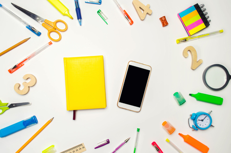 mobile phone and yellow notebook in the desk. white background. concept of education. back to school. creative mess on the desktop. desk. stationery. smartphone. place for text. flat lay.の写真素材
