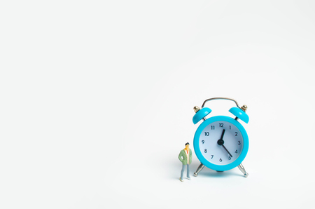 A man stands near a blue alarm clock and waits for someone. The concept of waiting for a meeting, a date. Late and punctual. The cost of hourly work of a specialist, business planning.の写真素材
