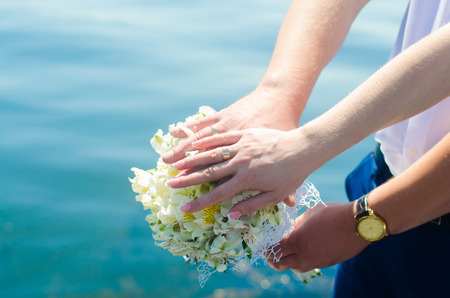 Close-up Bride and groom's hands with wedding rings and bouquet. Love and marriage. Wedding accessories and decor on the background of the riverの写真素材